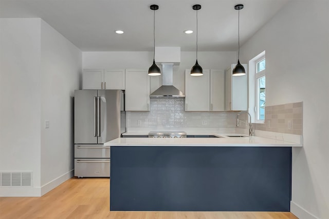 kitchen featuring visible vents, freestanding refrigerator, a sink, a peninsula, and wall chimney exhaust hood