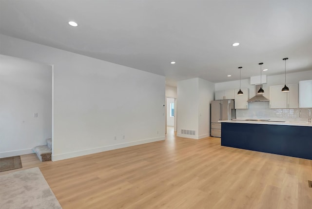 kitchen featuring high quality fridge, light wood-style floors, light countertops, decorative backsplash, and wall chimney exhaust hood