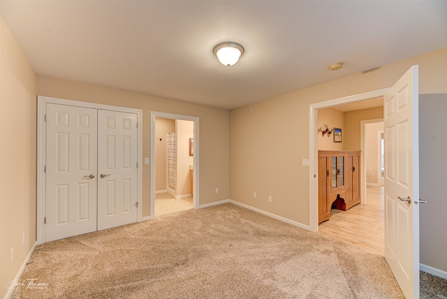 unfurnished bedroom with ensuite bathroom, light carpet, and a closet