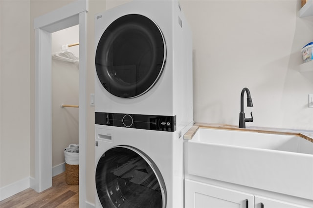 laundry area with cabinets, stacked washer and dryer, and light hardwood / wood-style flooring