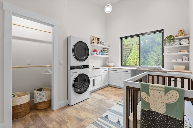 laundry area with light hardwood / wood-style floors, cabinets, and stacked washer and dryer