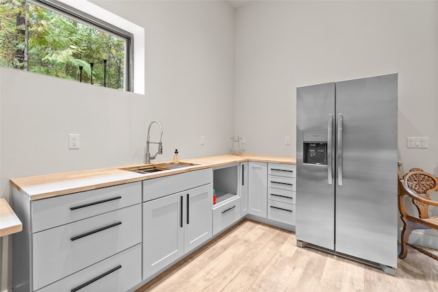 kitchen featuring stainless steel fridge, butcher block counters, light wood-type flooring, and sink