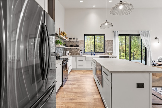 kitchen with tasteful backsplash, stainless steel appliances, decorative light fixtures, light hardwood / wood-style flooring, and white cabinets