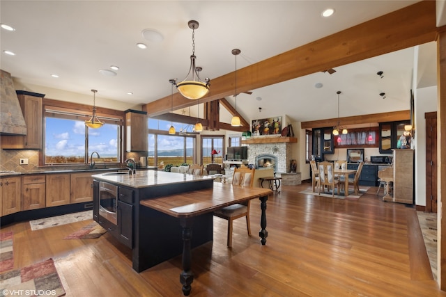 kitchen featuring a kitchen island with sink, dark wood-type flooring, a fireplace, hanging light fixtures, and a breakfast bar area