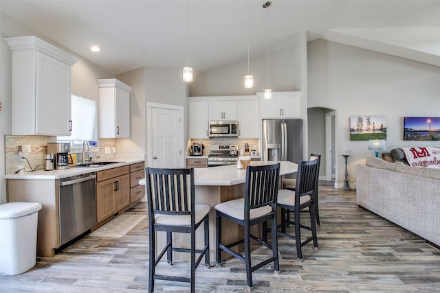 kitchen featuring a center island, sink, appliances with stainless steel finishes, decorative light fixtures, and white cabinetry