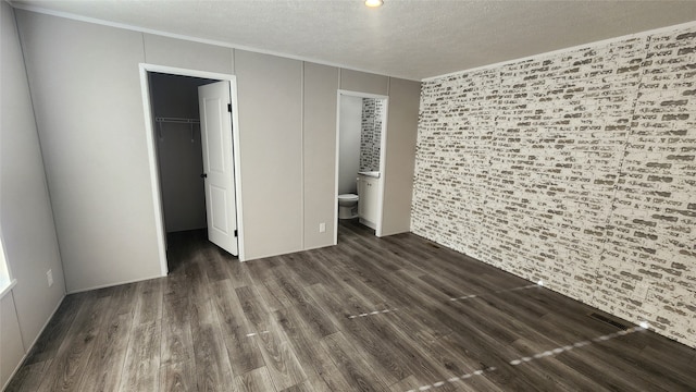 unfurnished bedroom with dark wood-type flooring, ensuite bath, a spacious closet, a textured ceiling, and a closet