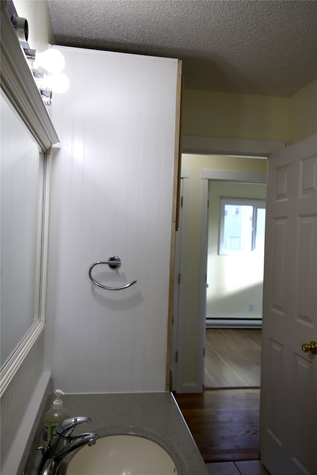 bathroom with vanity, a textured ceiling, hardwood / wood-style flooring, and a baseboard radiator