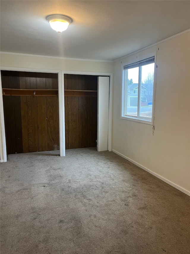 unfurnished bedroom with carpet, ornamental molding, and multiple closets