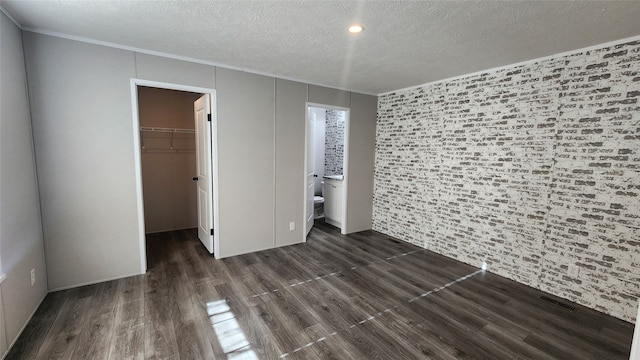 unfurnished bedroom featuring ensuite bath, a spacious closet, dark hardwood / wood-style flooring, a textured ceiling, and a closet