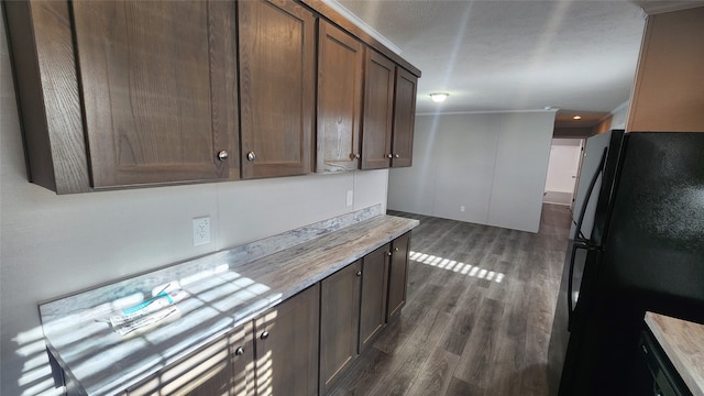 kitchen featuring dark brown cabinetry, crown molding, black refrigerator, and dark wood-type flooring