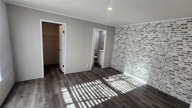 unfurnished bedroom with a walk in closet, ensuite bathroom, a closet, and dark wood-type flooring