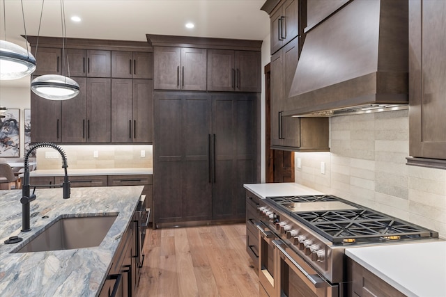 kitchen with light stone countertops, premium range hood, light hardwood / wood-style floors, sink, and stainless steel stove