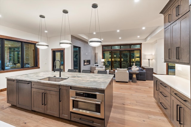 kitchen featuring light stone counters, sink, pendant lighting, light hardwood / wood-style floors, and oven