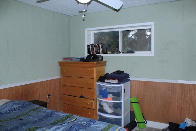 bedroom with ceiling fan and wood walls