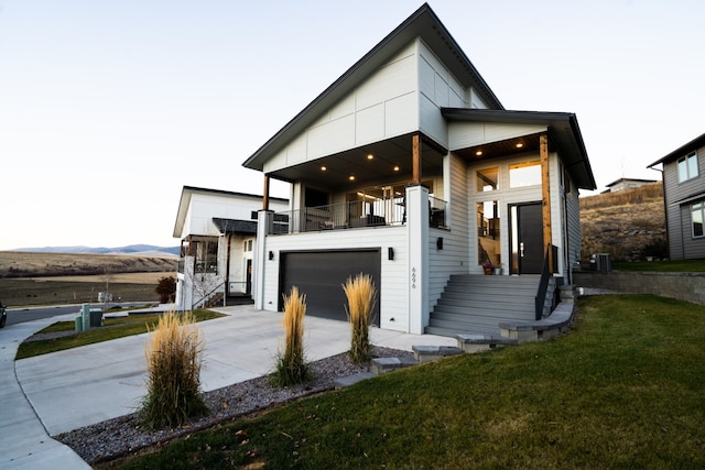 modern home with a balcony, central AC unit, a front yard, and a garage