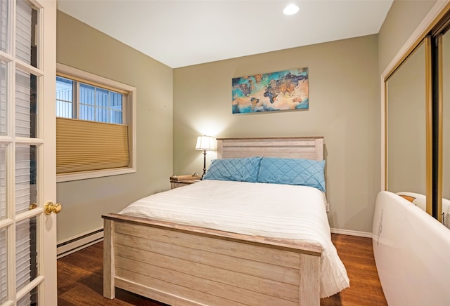 bedroom featuring a baseboard heating unit, dark wood-type flooring, and a closet