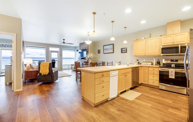 kitchen with kitchen peninsula, appliances with stainless steel finishes, light wood-type flooring, light brown cabinetry, and hanging light fixtures