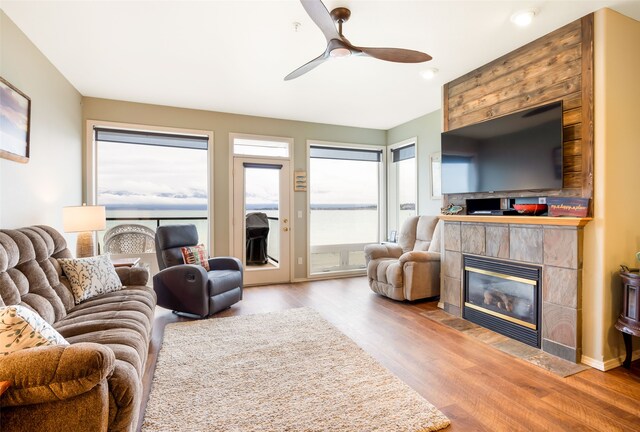 living room with ceiling fan, wood-type flooring, and a tile fireplace