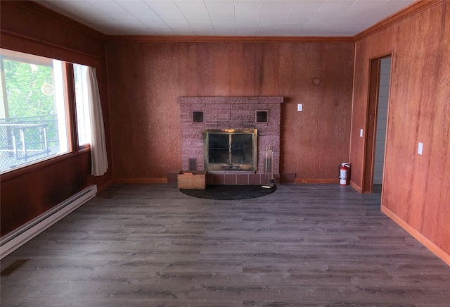 unfurnished living room with hardwood / wood-style floors, wood walls, a stone fireplace, and baseboard heating