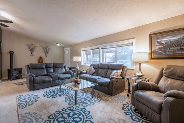 carpeted living room with vaulted ceiling, a wood stove, ceiling fan, and a textured ceiling