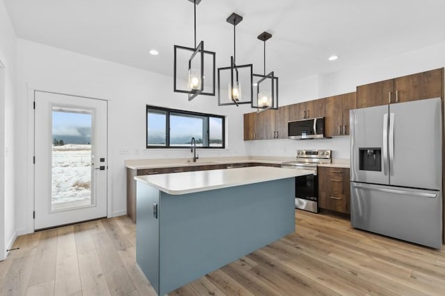 kitchen with appliances with stainless steel finishes, a center island, light hardwood / wood-style flooring, and hanging light fixtures