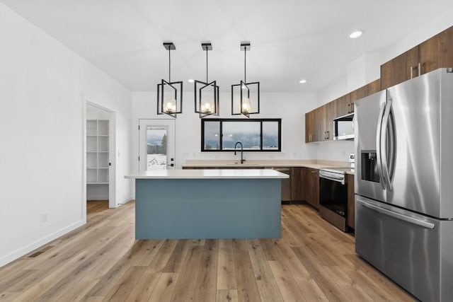 kitchen with appliances with stainless steel finishes, light wood-type flooring, a center island, and hanging light fixtures