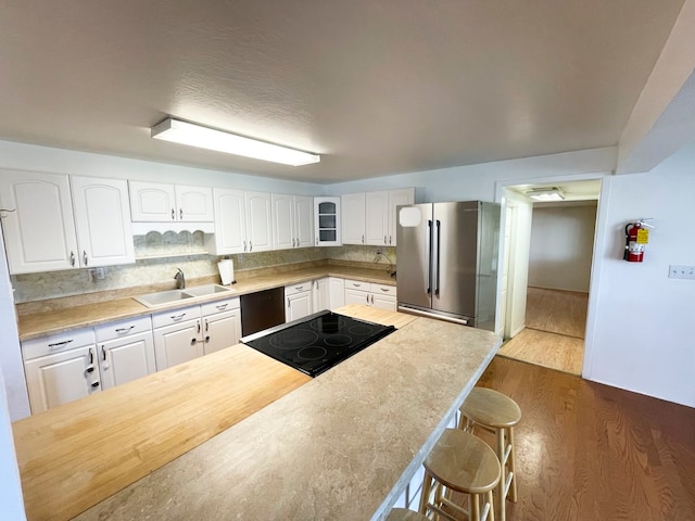 kitchen featuring white cabinetry, tasteful backsplash, wood-type flooring, a kitchen bar, and black appliances