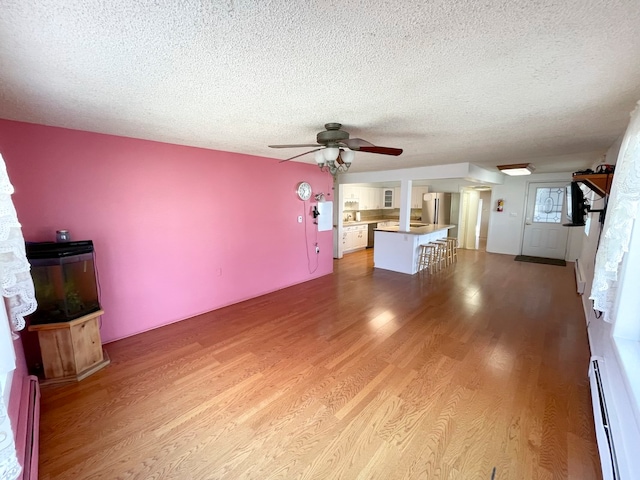 unfurnished living room with ceiling fan, a baseboard radiator, a textured ceiling, and hardwood / wood-style flooring