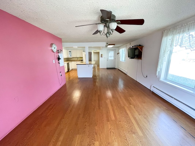 unfurnished living room with a textured ceiling, light wood-type flooring, ceiling fan, and a baseboard heating unit