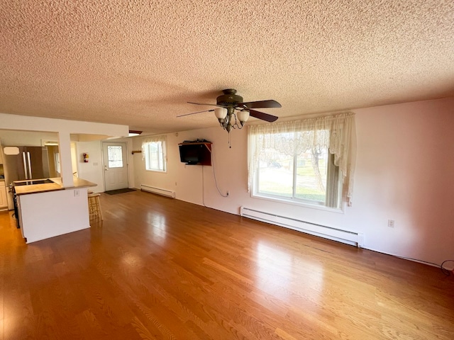 unfurnished living room featuring a healthy amount of sunlight, wood-type flooring, and baseboard heating