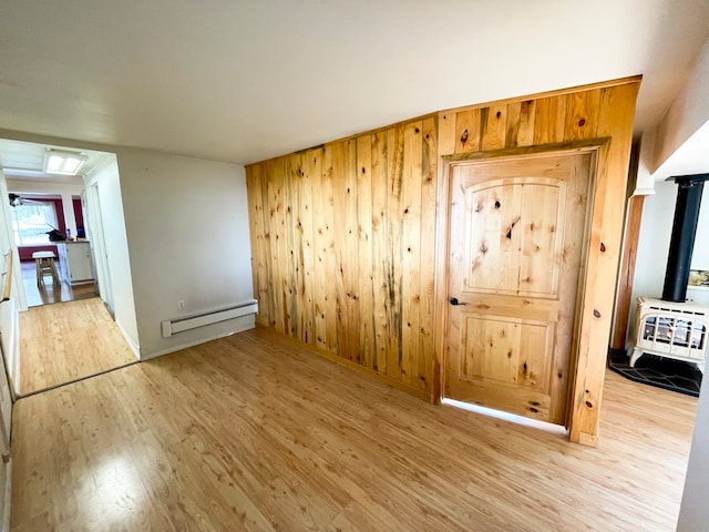 empty room with light hardwood / wood-style flooring, baseboard heating, and wooden walls