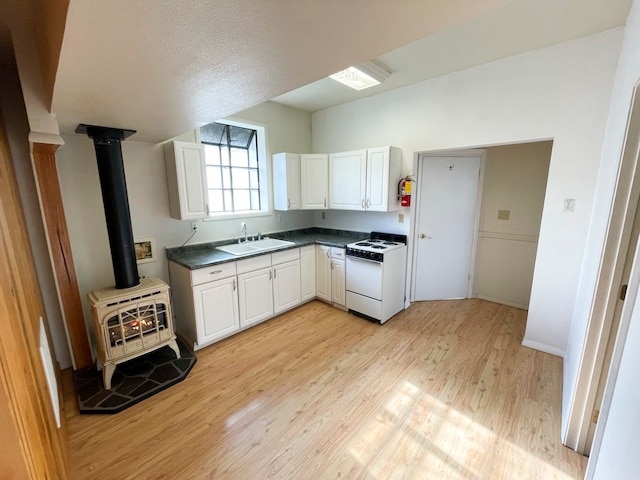 kitchen featuring a wood stove, white cabinetry, sink, light hardwood / wood-style flooring, and white range