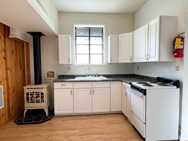 kitchen with white cabinets, white gas stove, light hardwood / wood-style floors, and a wood stove