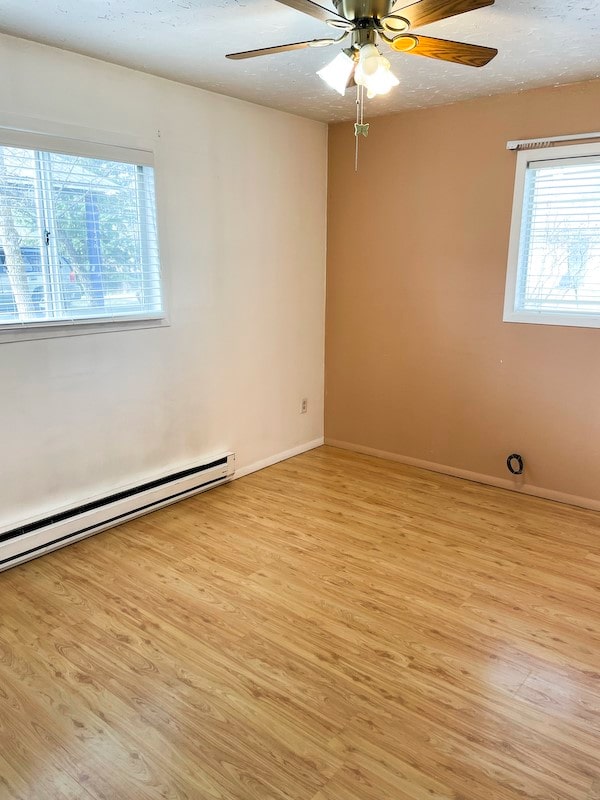 unfurnished room with ceiling fan, a baseboard radiator, a textured ceiling, and light wood-type flooring