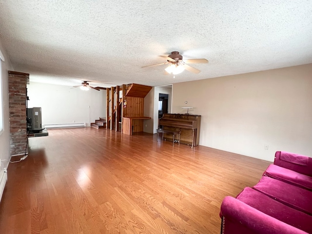 living room with a wood stove, hardwood / wood-style flooring, ceiling fan, a textured ceiling, and baseboard heating