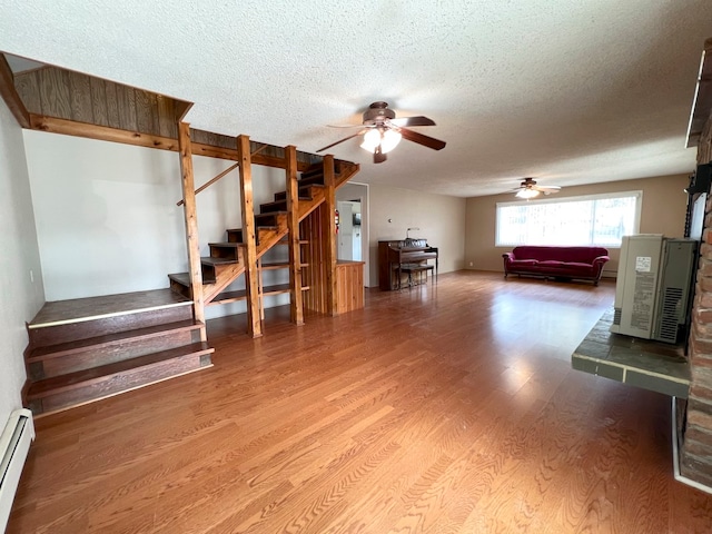 basement featuring wood-type flooring, a textured ceiling, ceiling fan, and a baseboard heating unit