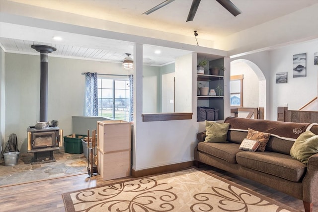 living room with ceiling fan, light wood-type flooring, a wood stove, and ornamental molding