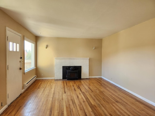 unfurnished living room with light wood-type flooring, baseboard heating, and a brick fireplace