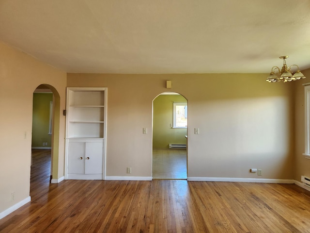 empty room with baseboard heating, built in features, light hardwood / wood-style floors, and an inviting chandelier