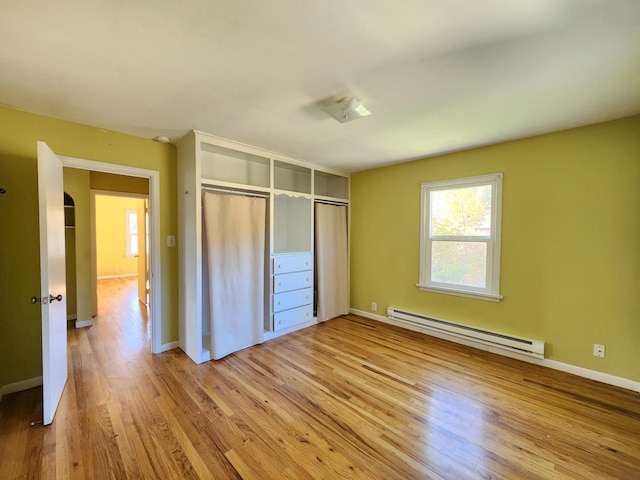 unfurnished bedroom with a closet, light wood-type flooring, and a baseboard heating unit