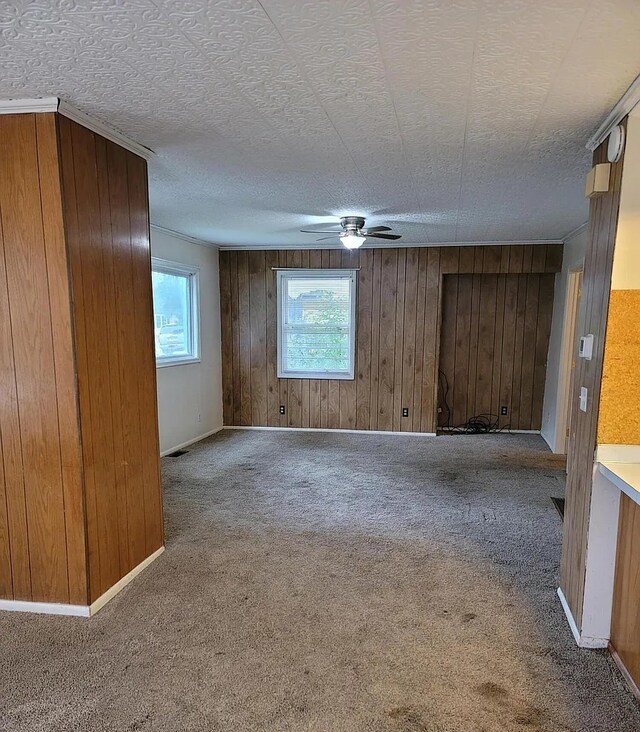 carpeted spare room featuring a textured ceiling, ceiling fan, and wood walls