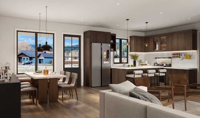 kitchen with dark wood-type flooring, decorative backsplash, decorative light fixtures, a kitchen bar, and stainless steel refrigerator