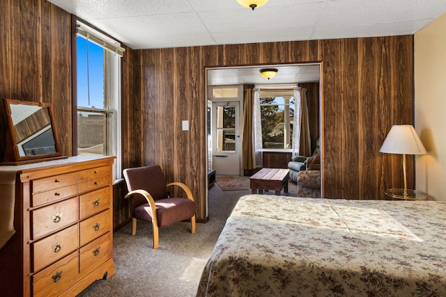 bedroom featuring wood walls, dark carpet, and multiple windows