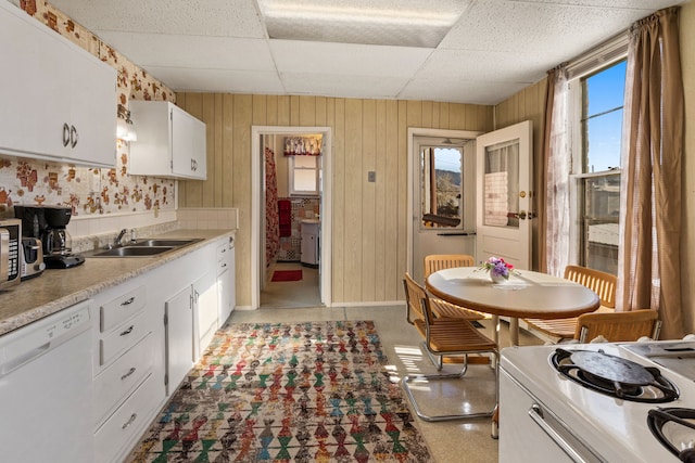 kitchen with a drop ceiling, sink, wood walls, white appliances, and white cabinets