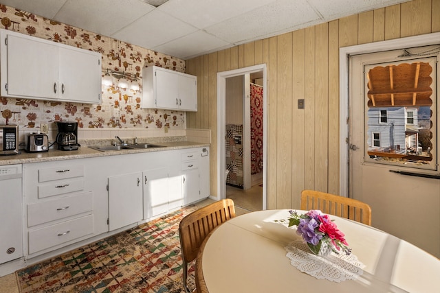 kitchen featuring a paneled ceiling, white cabinetry, sink, and wooden walls