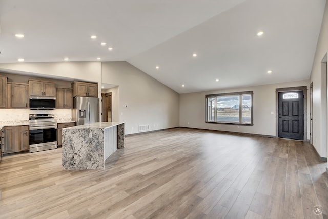 kitchen with a kitchen bar, appliances with stainless steel finishes, light stone counters, light hardwood / wood-style floors, and a kitchen island