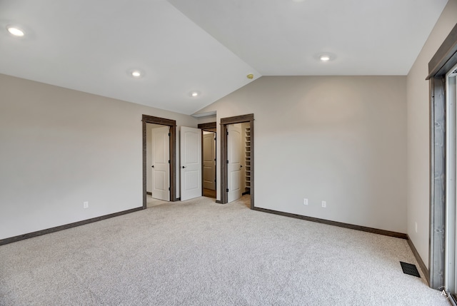 unfurnished bedroom with a closet, a spacious closet, light carpet, and vaulted ceiling