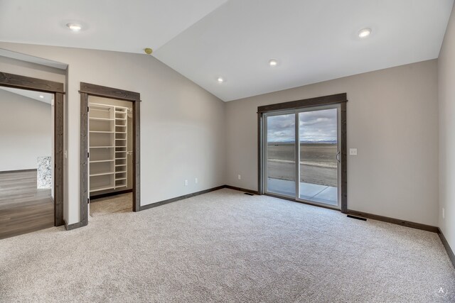 unfurnished bedroom with access to outside, a walk in closet, vaulted ceiling, light colored carpet, and a closet