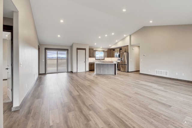 unfurnished living room with light hardwood / wood-style floors, high vaulted ceiling, and sink