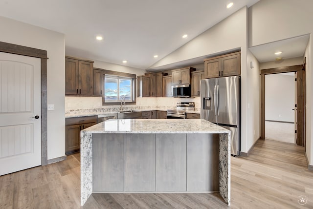 kitchen with a center island, stainless steel appliances, light stone counters, and light hardwood / wood-style floors